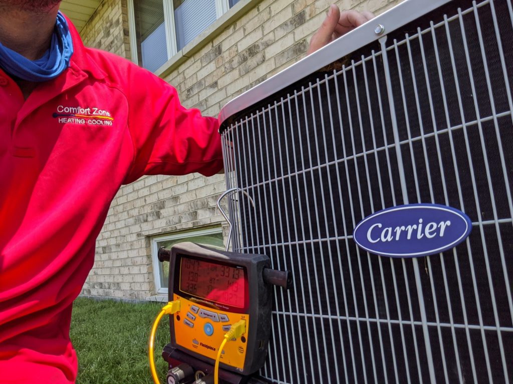 Comfort Zone Service technician performing AC maintenance on outdoor Carrier AC unit.