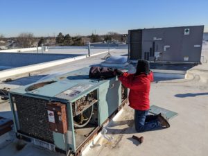 Comfort Zone technician working on commercial HVAC unit on a flat rooftop.