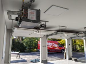 Comfort Zone Service technicians installing hanging garage heater in a three-car garage with doors open
