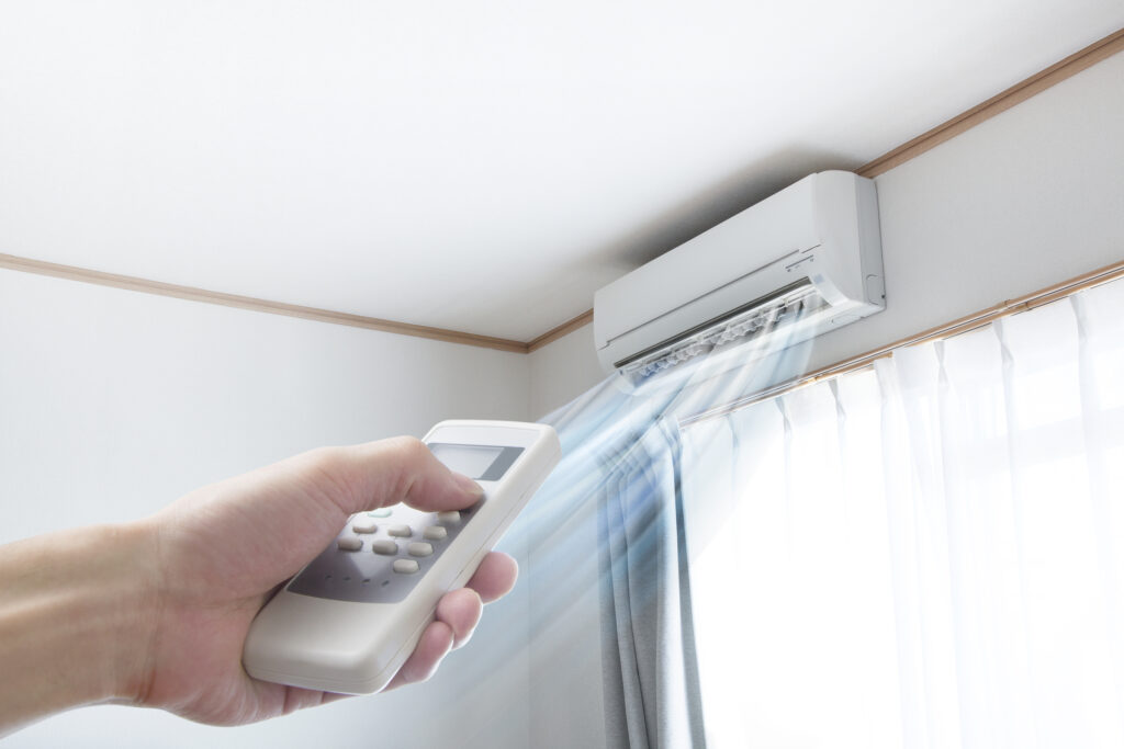 Hand pointing remote at the ductless mini-split installed over the window to change the temperature.